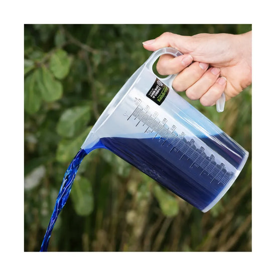 Hand pouring blue liquid from BAINBRIDGE chemical measuring jug with easy-grip handle and measurement markings