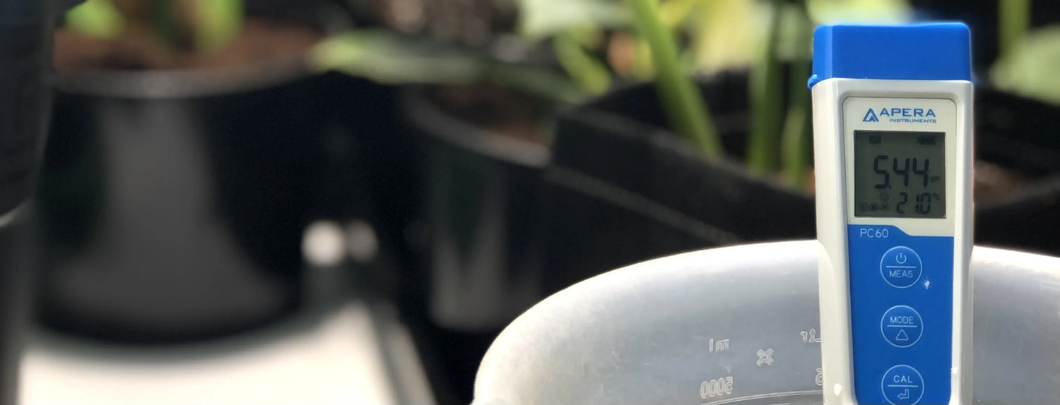 Digital pH and EC meter testing hydroponic nutrient solution in reservoir, monitoring water quality for optimal plant growth