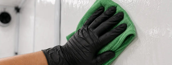 Gloved hand using isopropyl alcohol to sterilise grow room wall surface